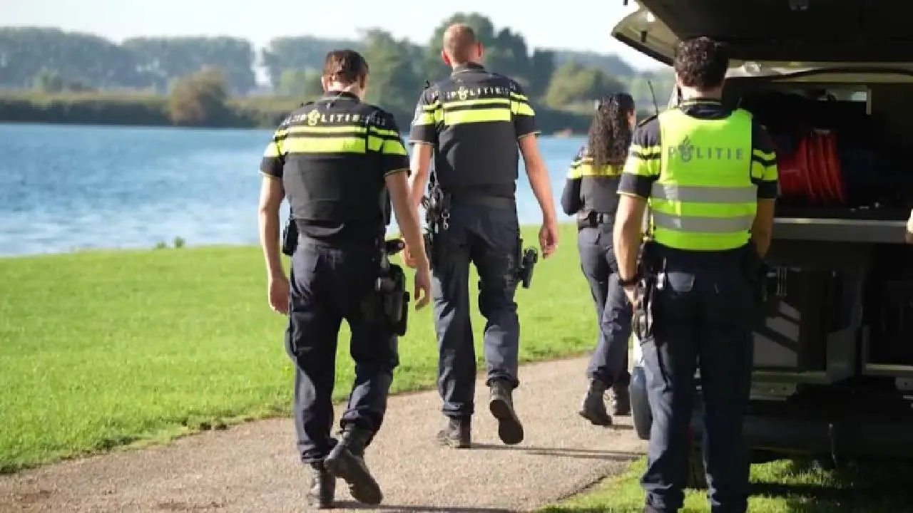 Politieagenten lopen langs een plas naar een politievoertuig